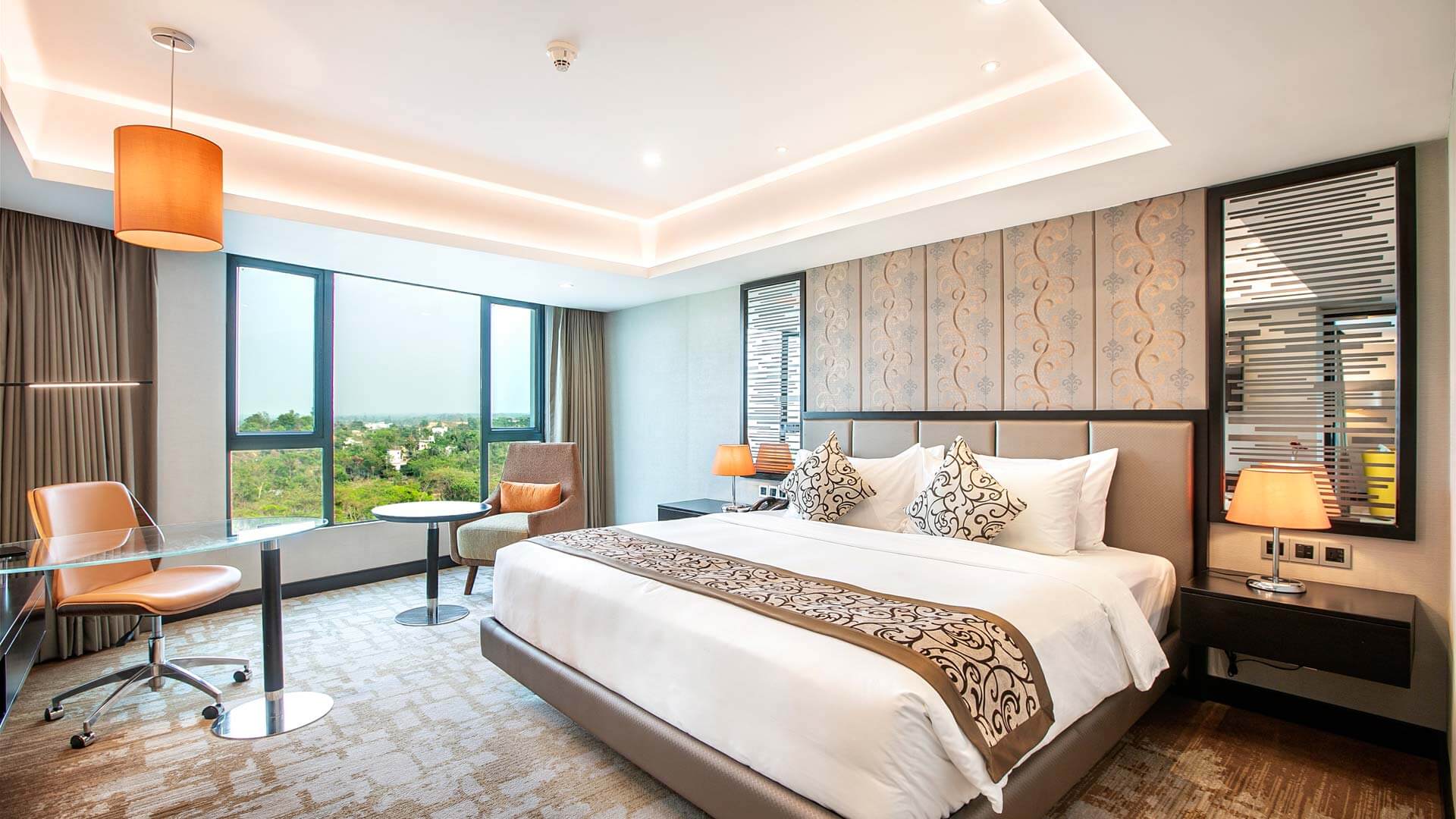 Deluxe king room with a warm-lit ceiling, patterned headboard wall and wide windows over the treetops