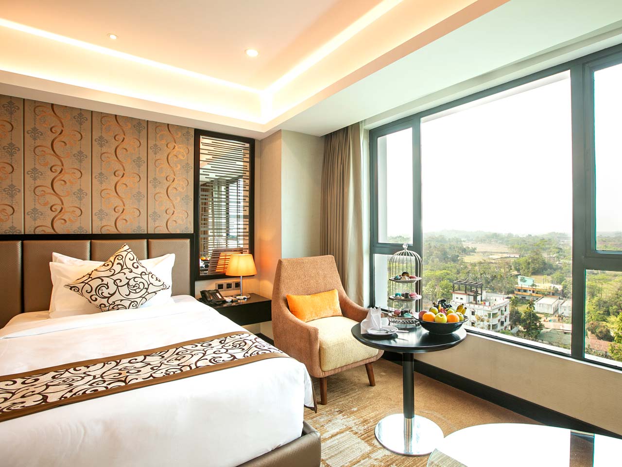 Twin room with an armchair and fruit table beside a corner window